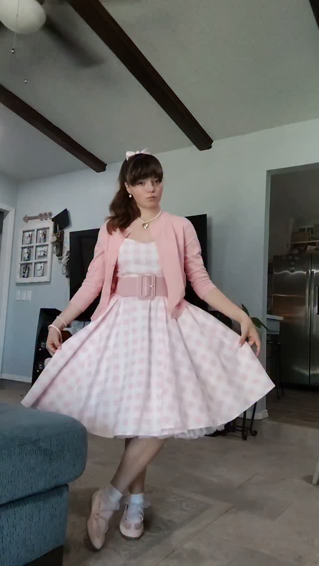 1950s Day Dress Ideas: 6 Retro Looks, From Gingham to Florals 6 Woman in a pink checkered 1950s day dress and cardigan posing indoors.