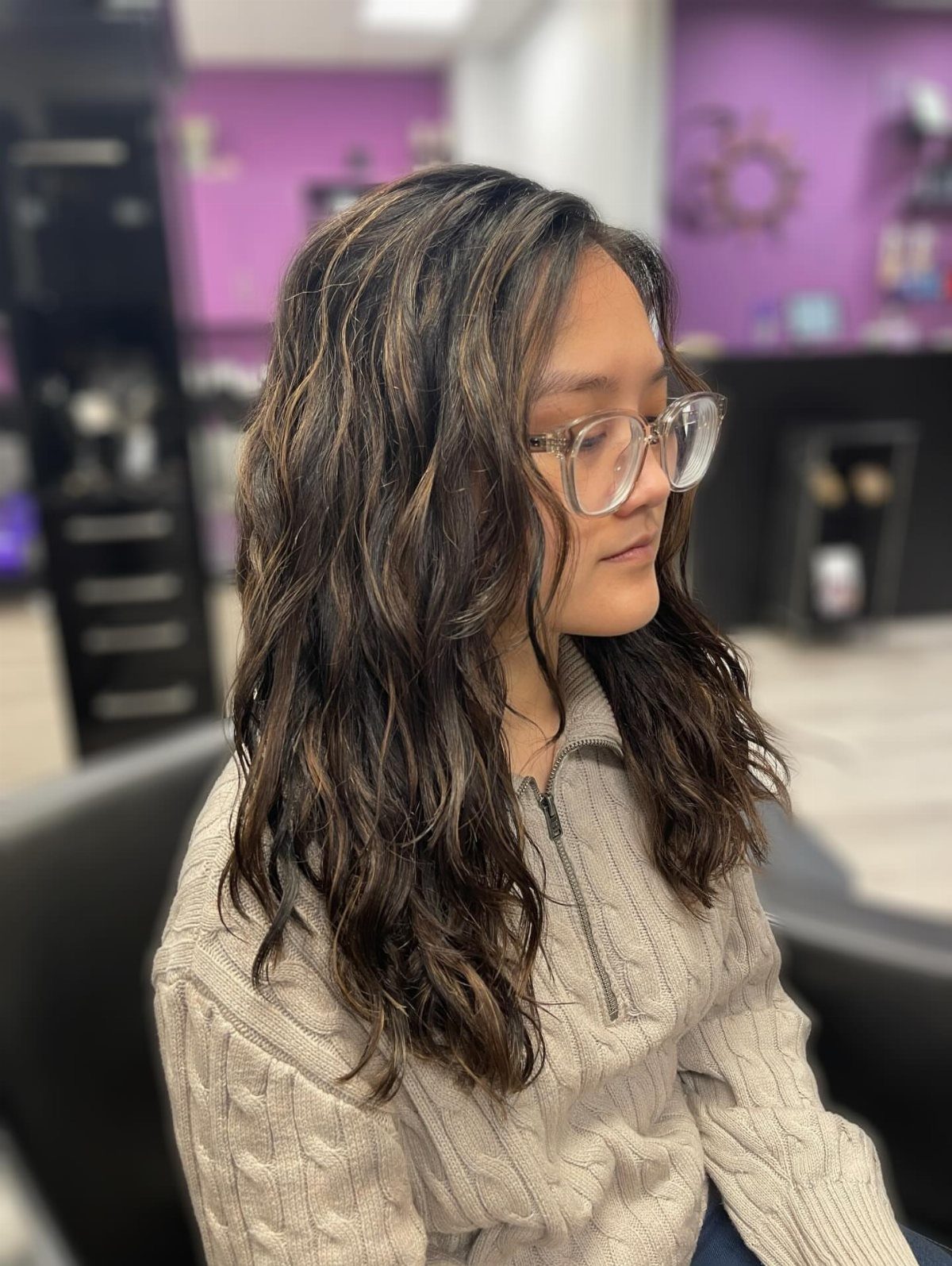 Woman with wavy brown hair and glasses wearing a beige cable-knit sweater.