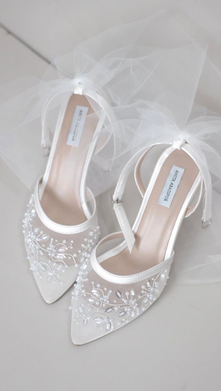 White pointed-toe wedding heels with beaded floral embellishments and sheer mesh panels.