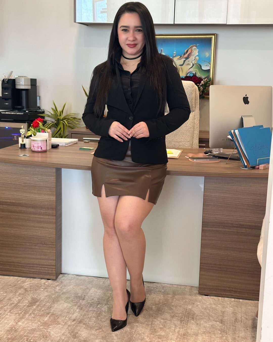 Woman in black blazer and brown leather skirt standing in an office setting