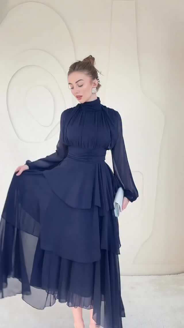 Woman in a navy blue high-neck dress with a flowy tiered skirt.