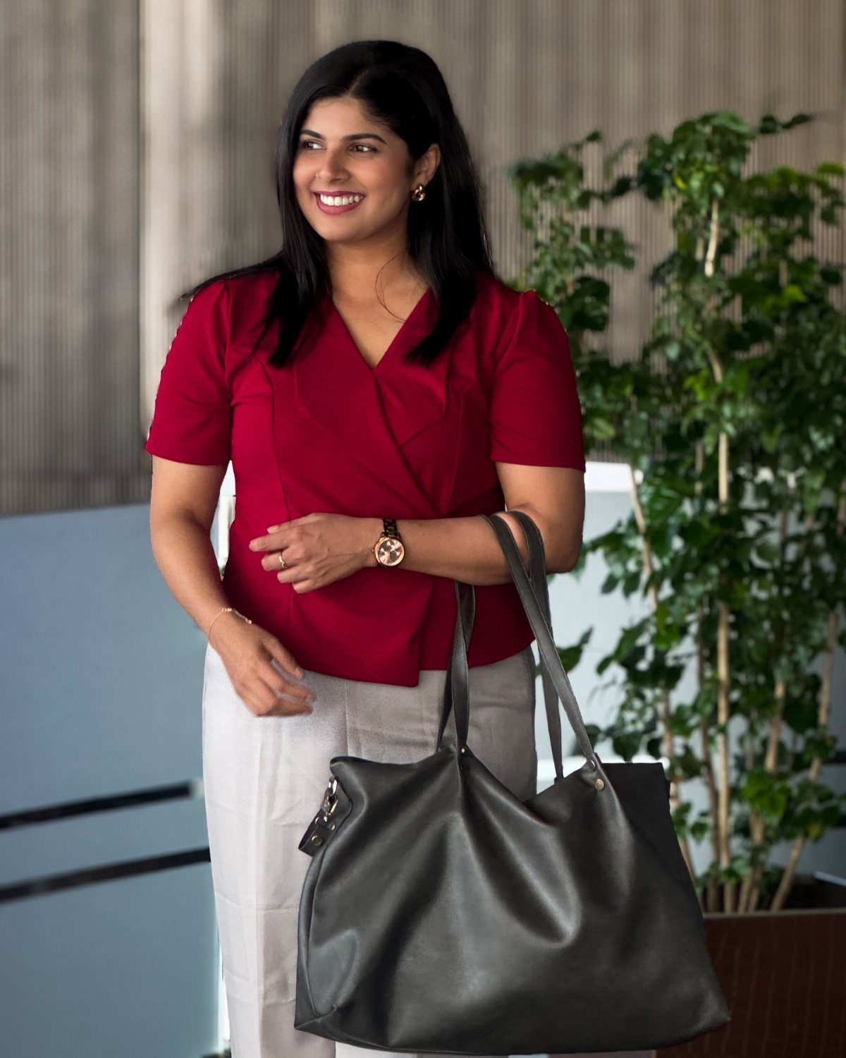 Woman wearing a red wrap blouse and white trousers holding a grey tote bag