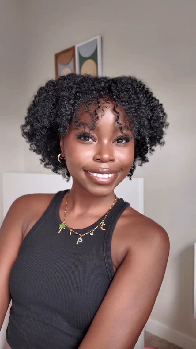 Woman with voluminous curly black hair wearing a black tank top and gold necklace.