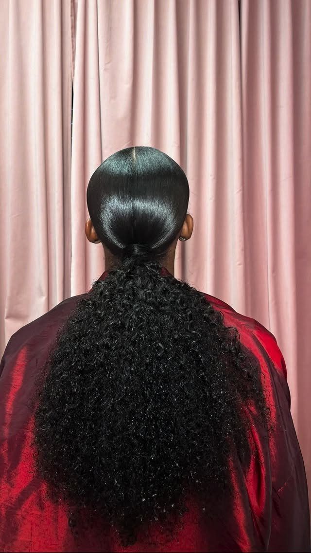Low ponytail with sleek top and voluminous 4c curls against pink curtains
