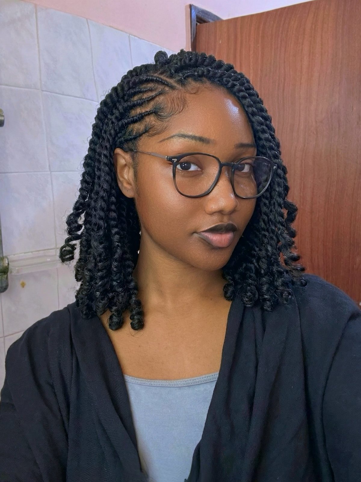 Woman with shoulder-length black twists and braided roots wearing black glasses and cardigan.