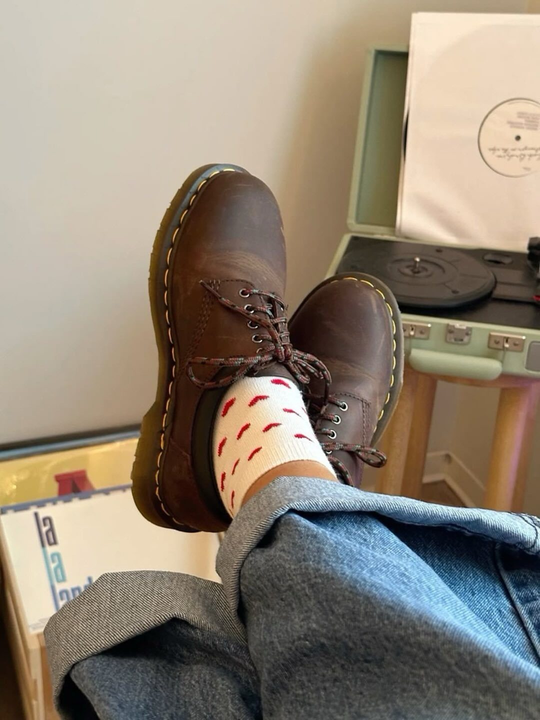 Brown leather platform shoes with yellow stitching worn with blue jeans and patterned socks.