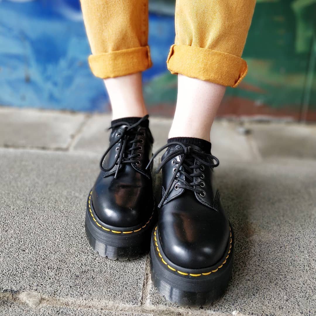 Black leather platform shoes with yellow stitching paired with mustard-yellow cuffed trousers.