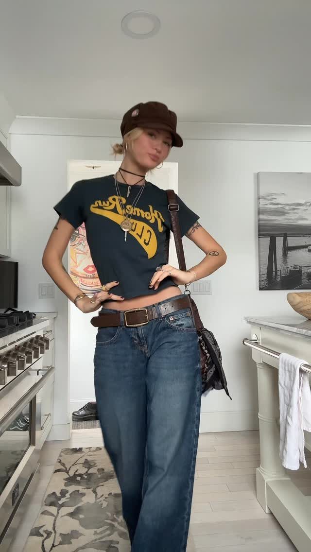 90s Vintage Streetwear Ideas: 9 Pieces Worth Wearing 7 Woman wearing baggy blue denim jeans, a cropped graphic tee, and brown cap.