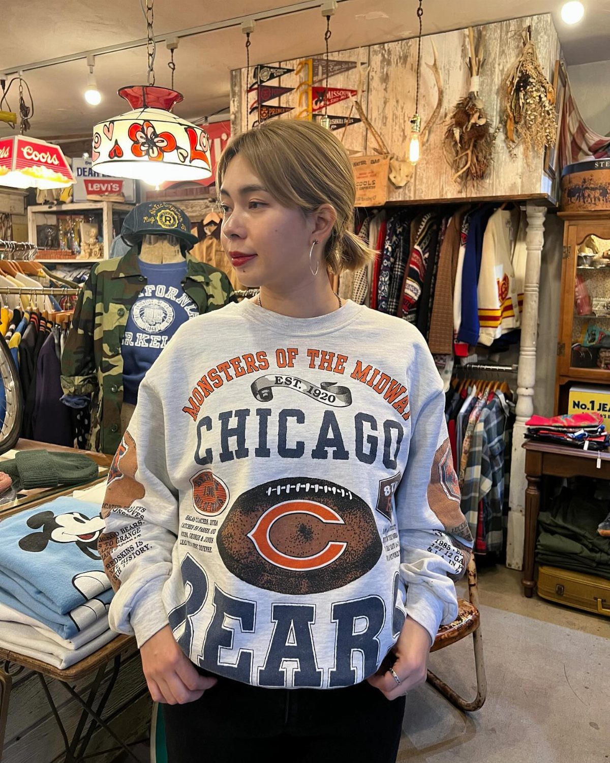 90s Vintage Streetwear Ideas: 9 Pieces Worth Wearing 4 Woman wearing a grey Chicago Bears graphic sweatshirt in a vintage clothing store.