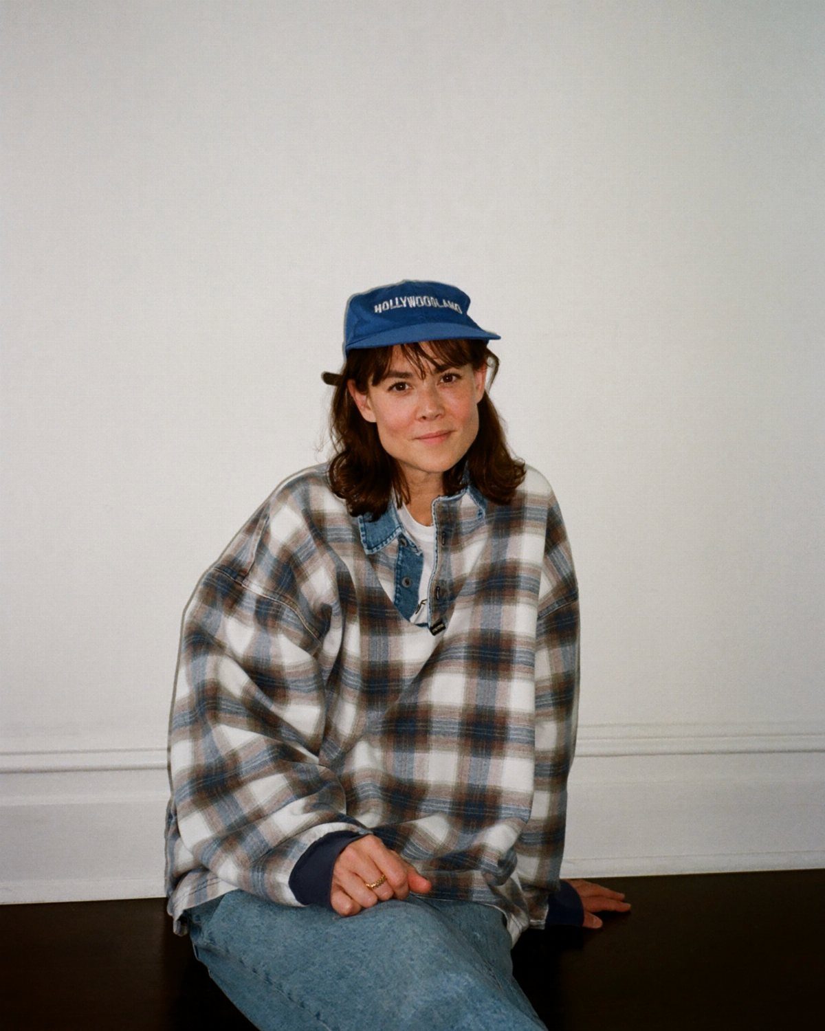 90s Vintage Streetwear Ideas: 9 Pieces Worth Wearing 2 Person wearing a blue baseball cap and oversized plaid flannel shirt sitting indoors.