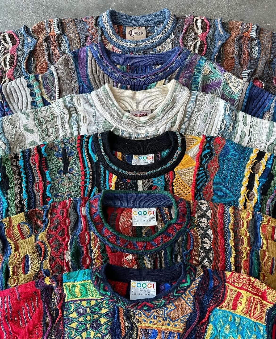 90s Vintage Streetwear Ideas: 9 Pieces Worth Wearing 9 Six colorful, textured knit sweaters with bold patterns layered on a grey surface.
