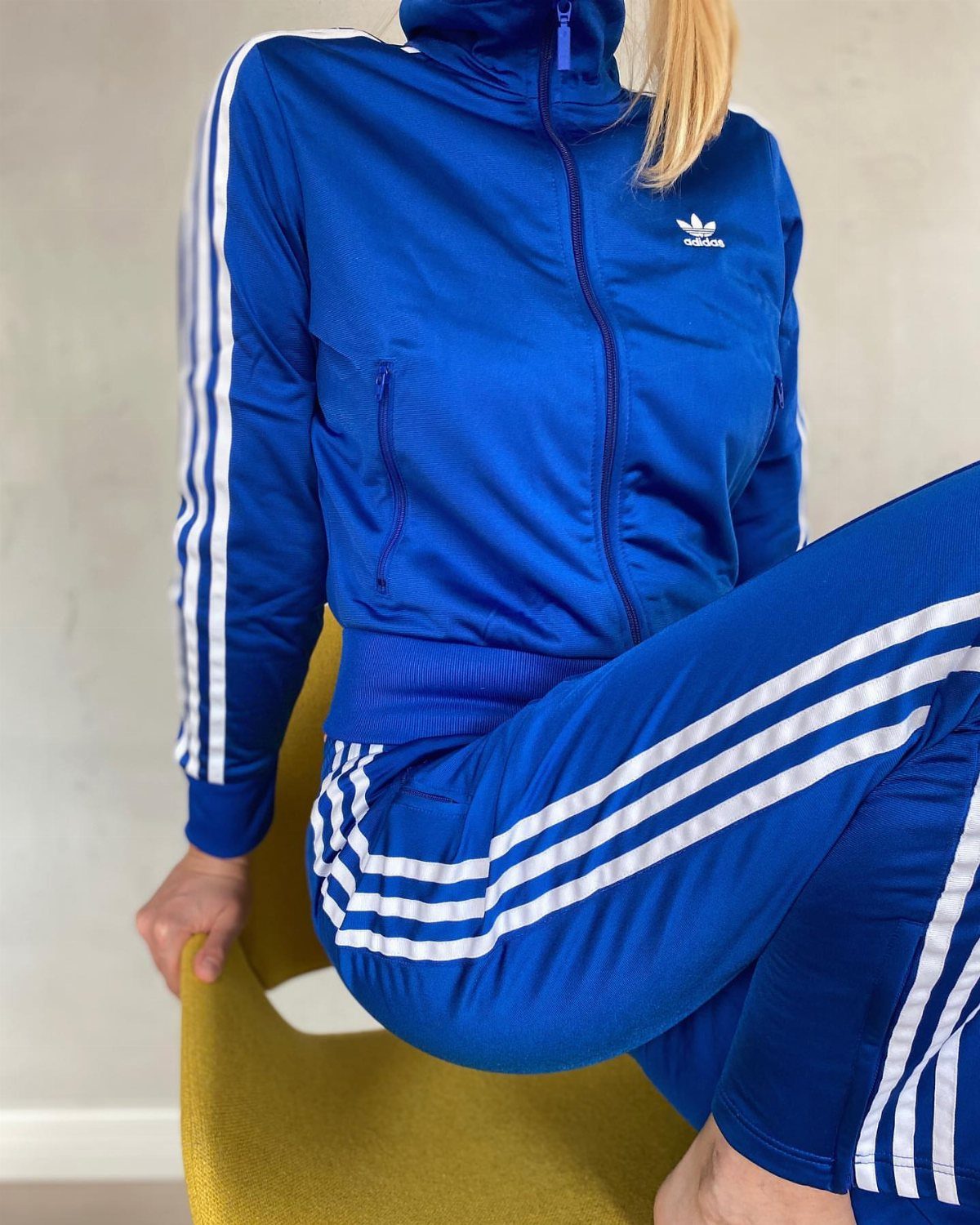 Person wearing a bright blue Adidas tracksuit with white stripes sitting on yellow chair