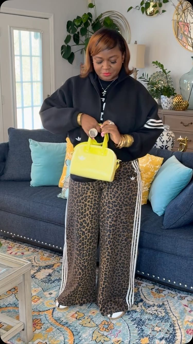 Woman wearing black Adidas jacket and leopard print track pants with yellow handbag.