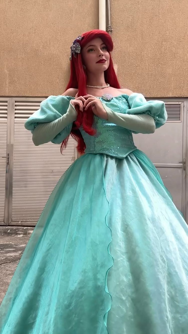 Woman with red hair wearing a teal Ariel princess ball gown and pearls.
