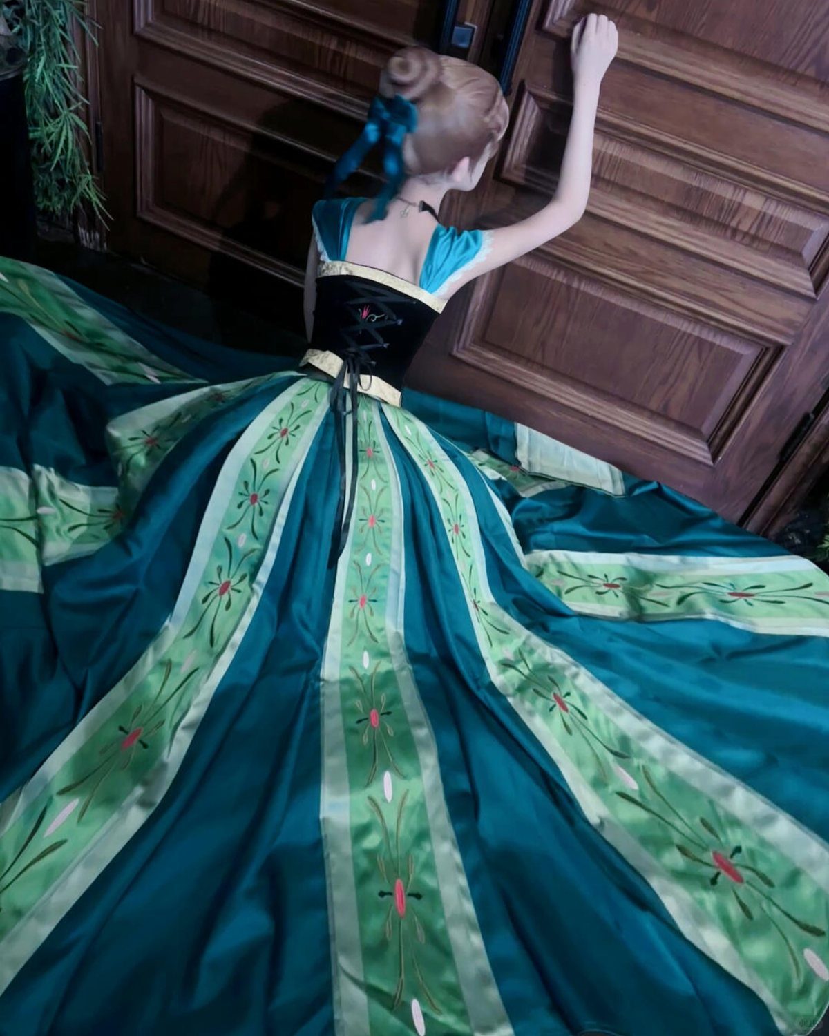 Woman in a teal and green Tiana princess gown standing by a wooden door