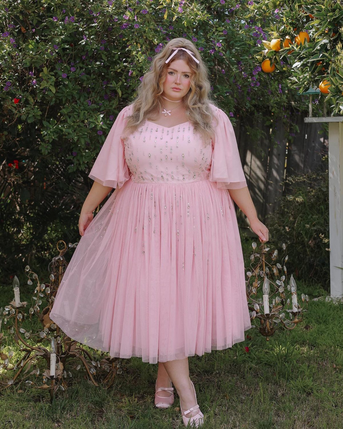 Plus-size woman in a pink sparkly princess dress standing in a lush garden