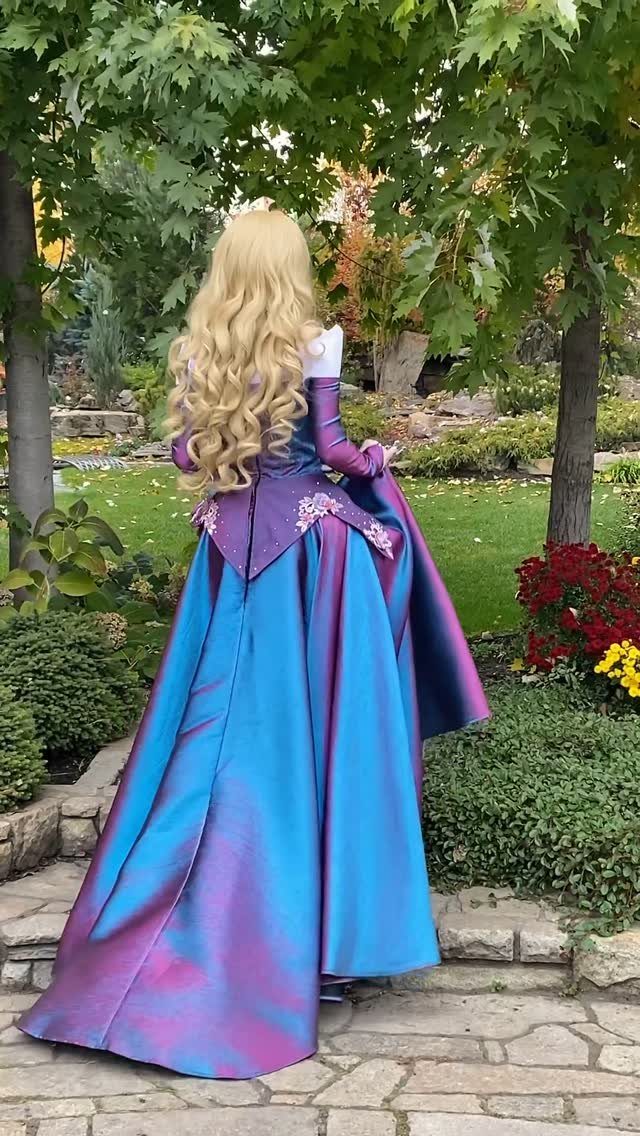Woman in a blue and purple iridescent Aurora princess gown standing in a garden