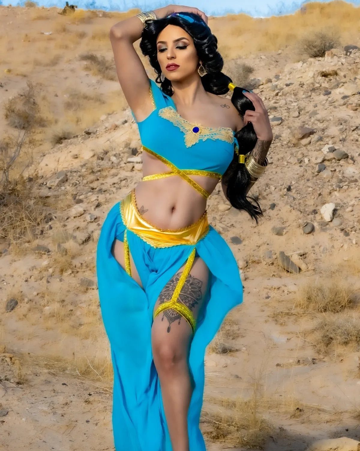 Woman in turquoise and gold Jasmine costume posing in a sandy desert landscape