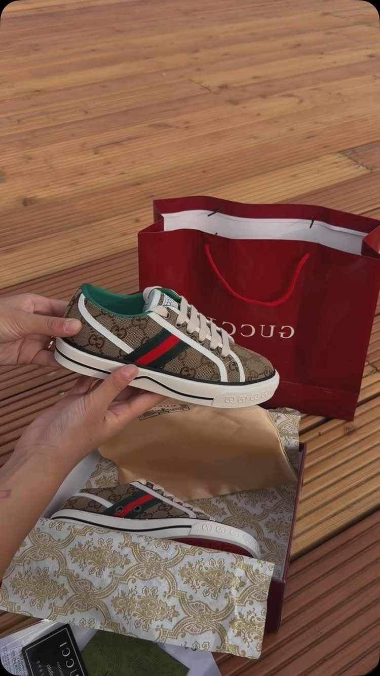 Brown patterned canvas sneakers with red and green stripes held over a box.