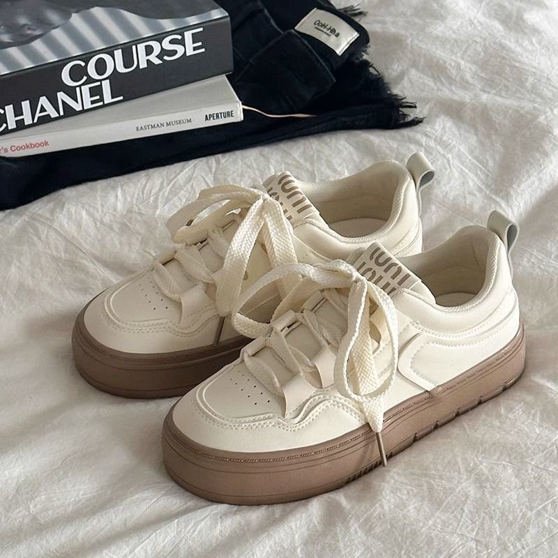 Off-white sneakers with tan soles resting on white fabric next to books.