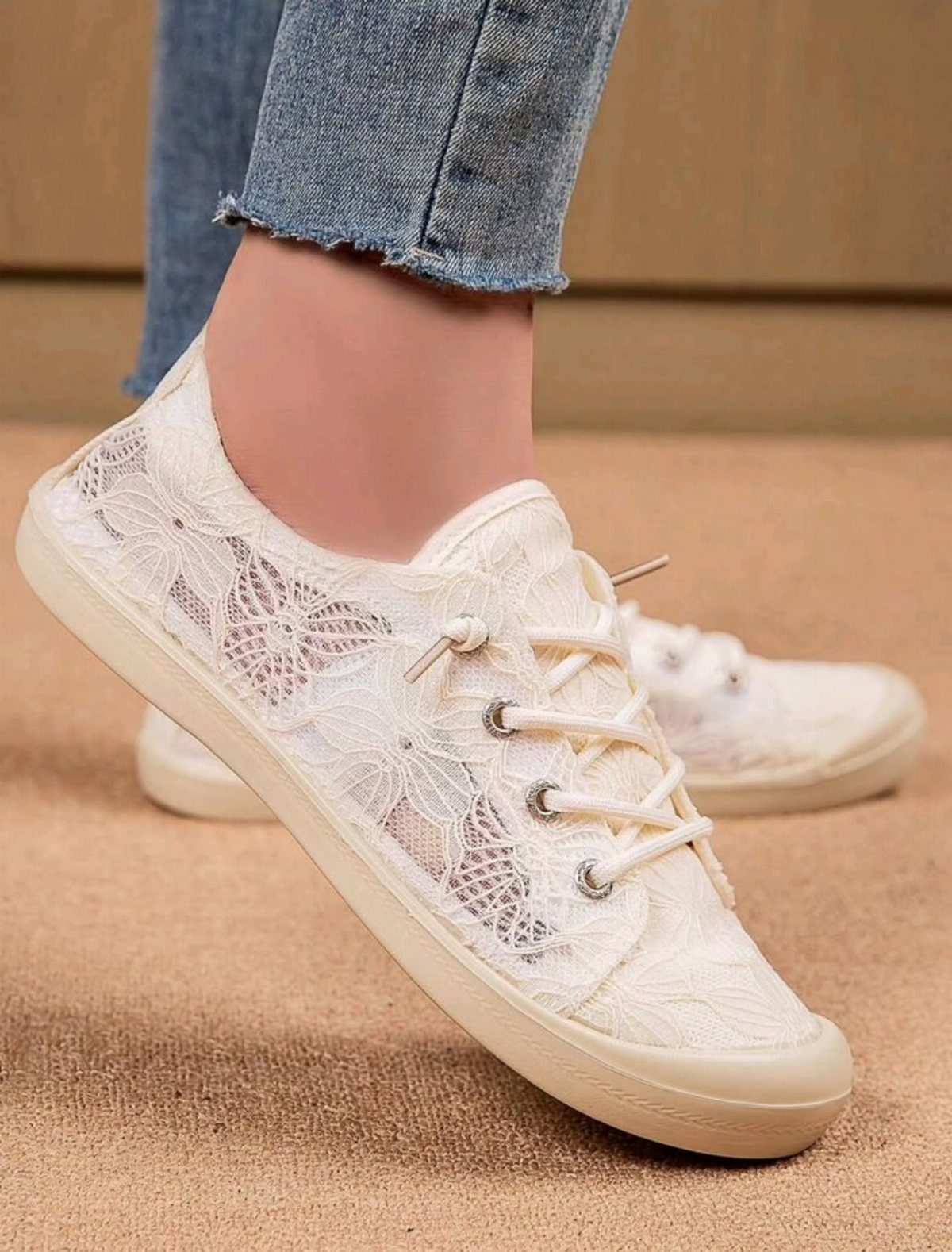 White lace sneakers with thin soles worn with blue denim jeans.