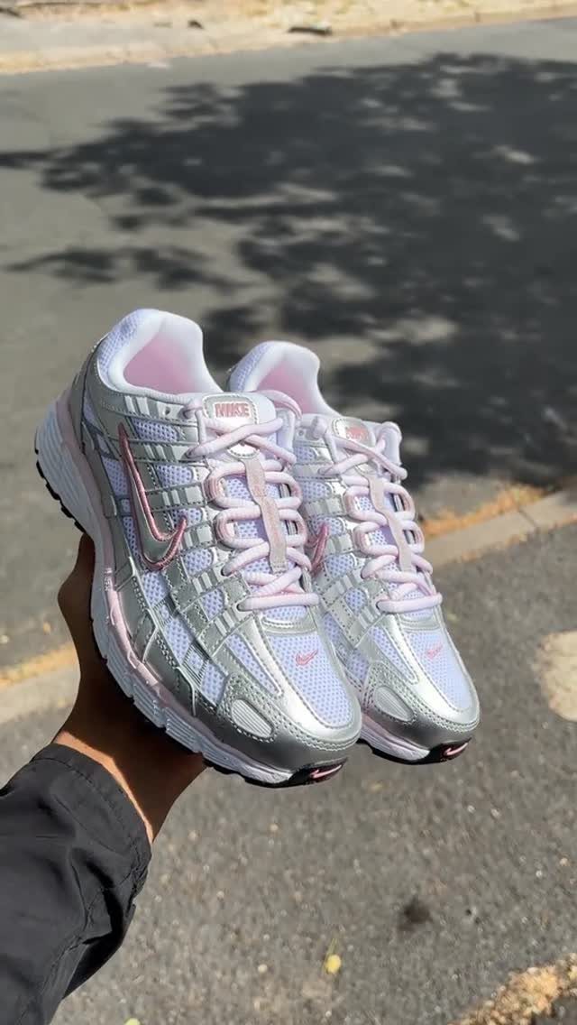 Silver and pink Nike sneakers held up against a blurred asphalt road background.