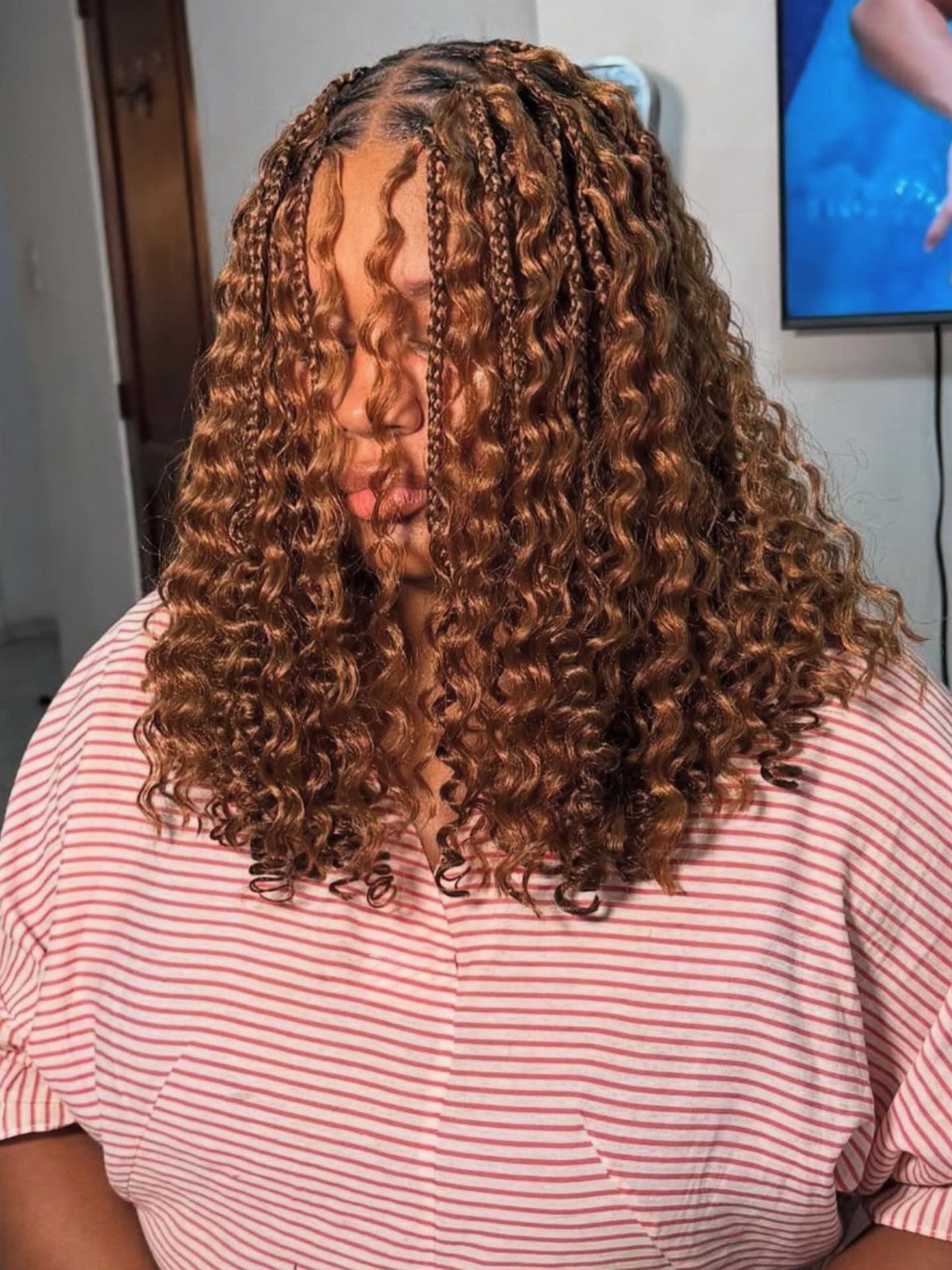 20 African Hair Styles Braids 12 Person with light brown crochet braids and curly ends wearing striped shirt