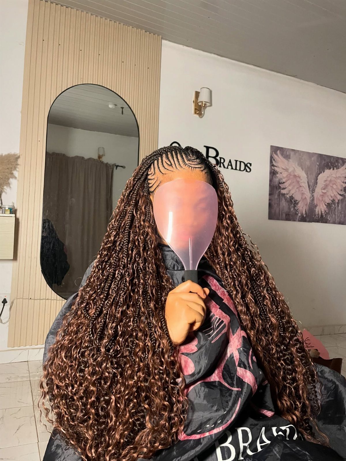 20 African Hair Styles Braids 4 Person with brown Fulani braids and curly ends holding a pink mirror.