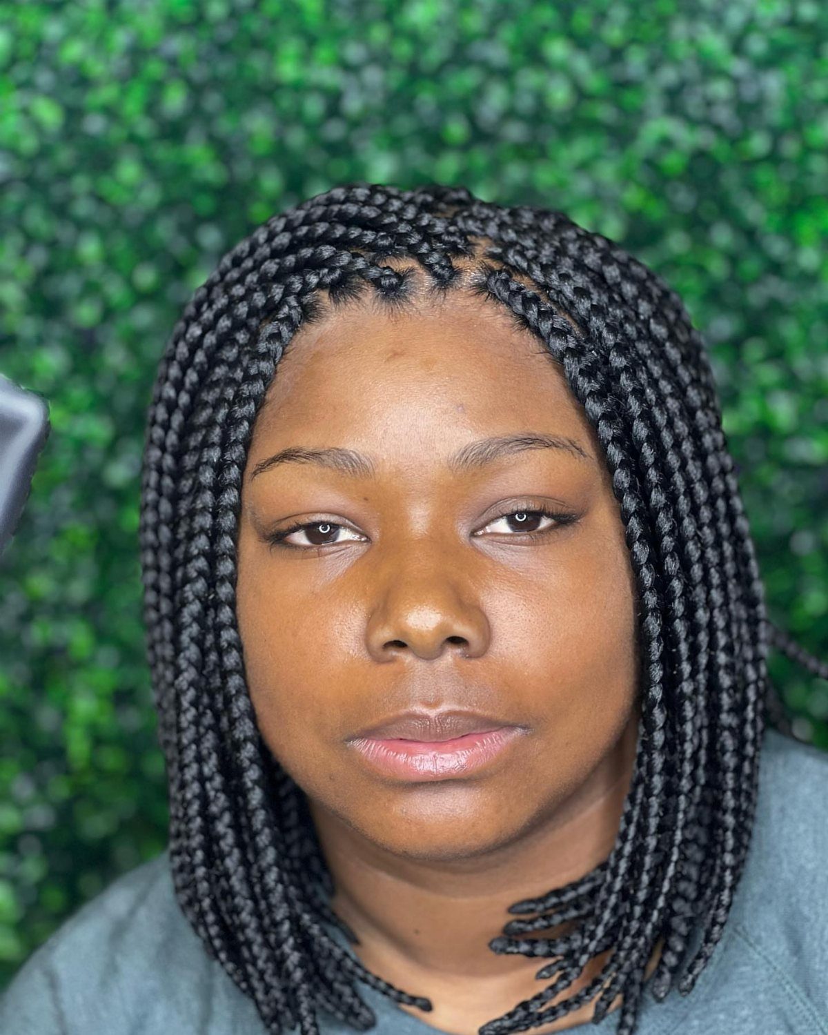 20 African Hair Styles Braids 9 Woman with black micro braids styled in a bob against a green hedge.