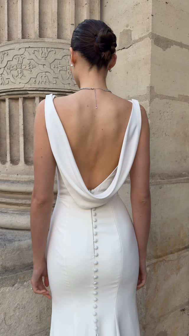 Woman in a white wedding dress with a dramatic cowl back and buttons.
