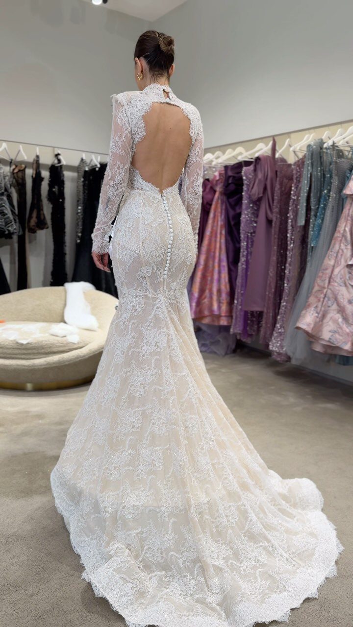 Woman wearing a white floral lace wedding dress with long sleeves and open back.