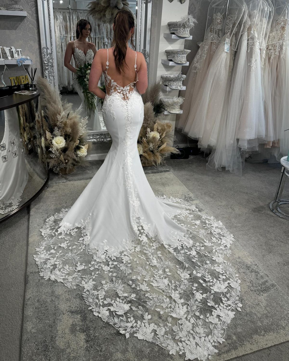 Woman wearing a white mermaid-style wedding dress with a long floral lace train.