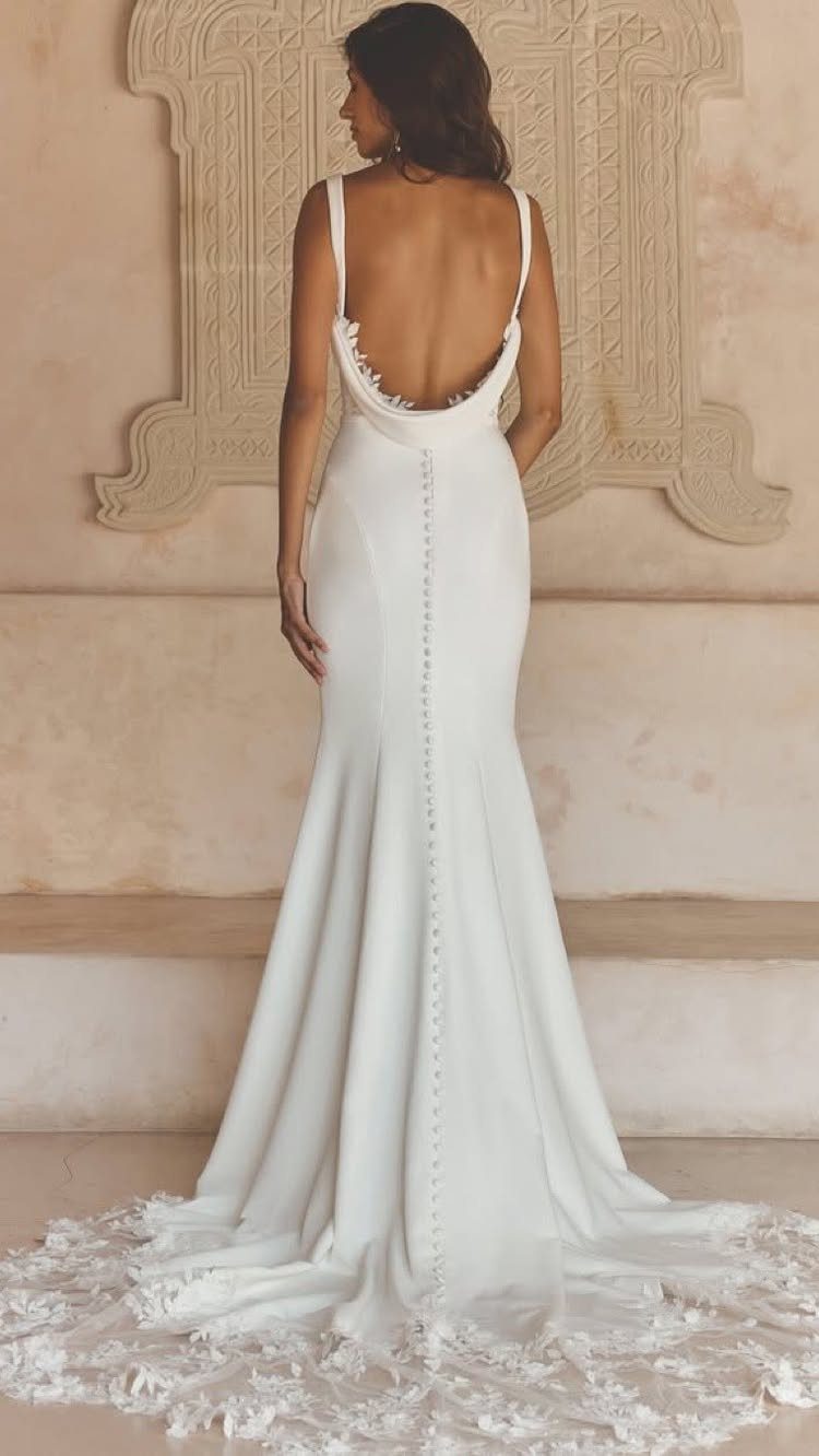 Woman in a white backless wedding dress with thin straps and button details.