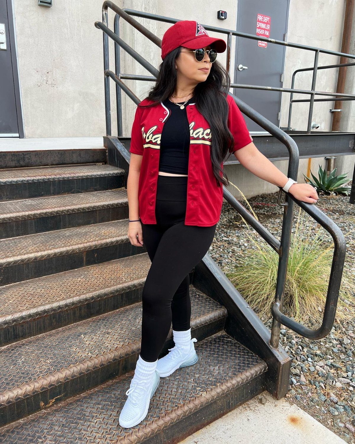 Woman wearing a red baseball jersey, black leggings, and a red baseball cap.