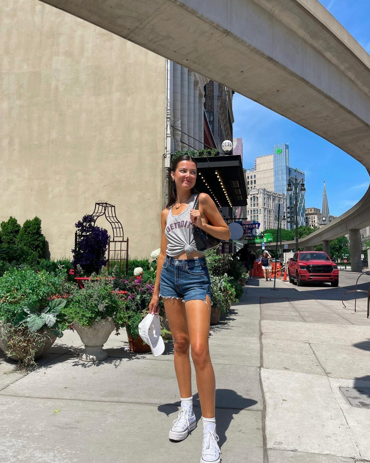 Woman wearing a grey graphic tee and denim shorts on a city sidewalk.