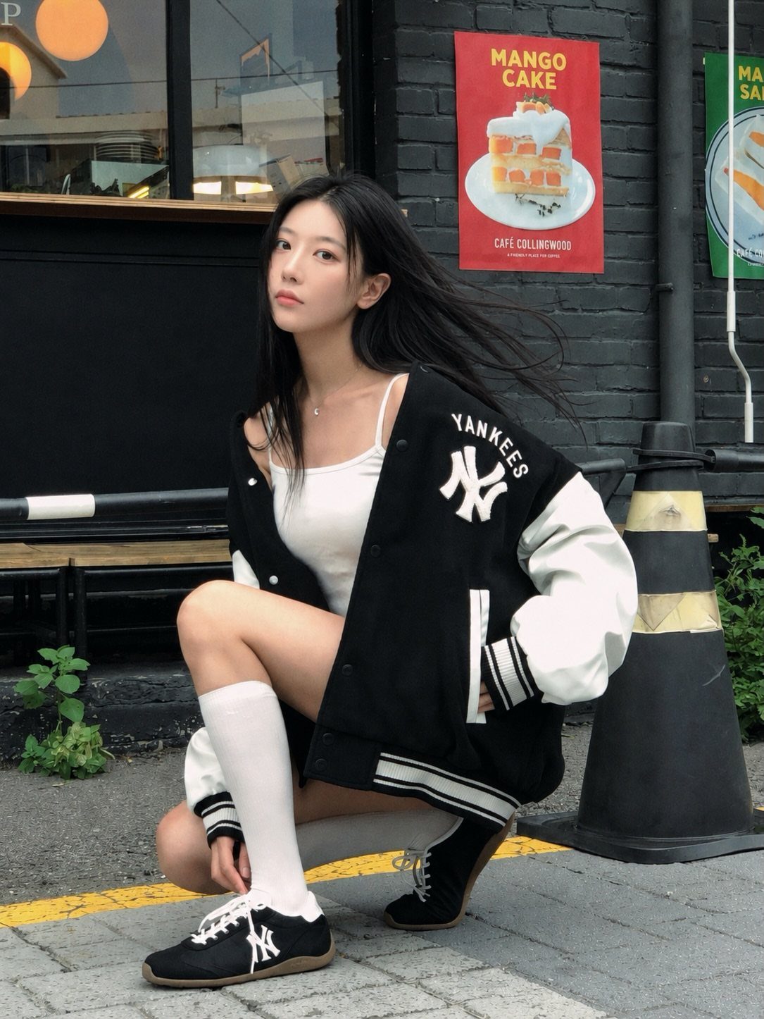 Woman wearing a New York Yankees varsity jacket, white tank top, and knee-high socks.
