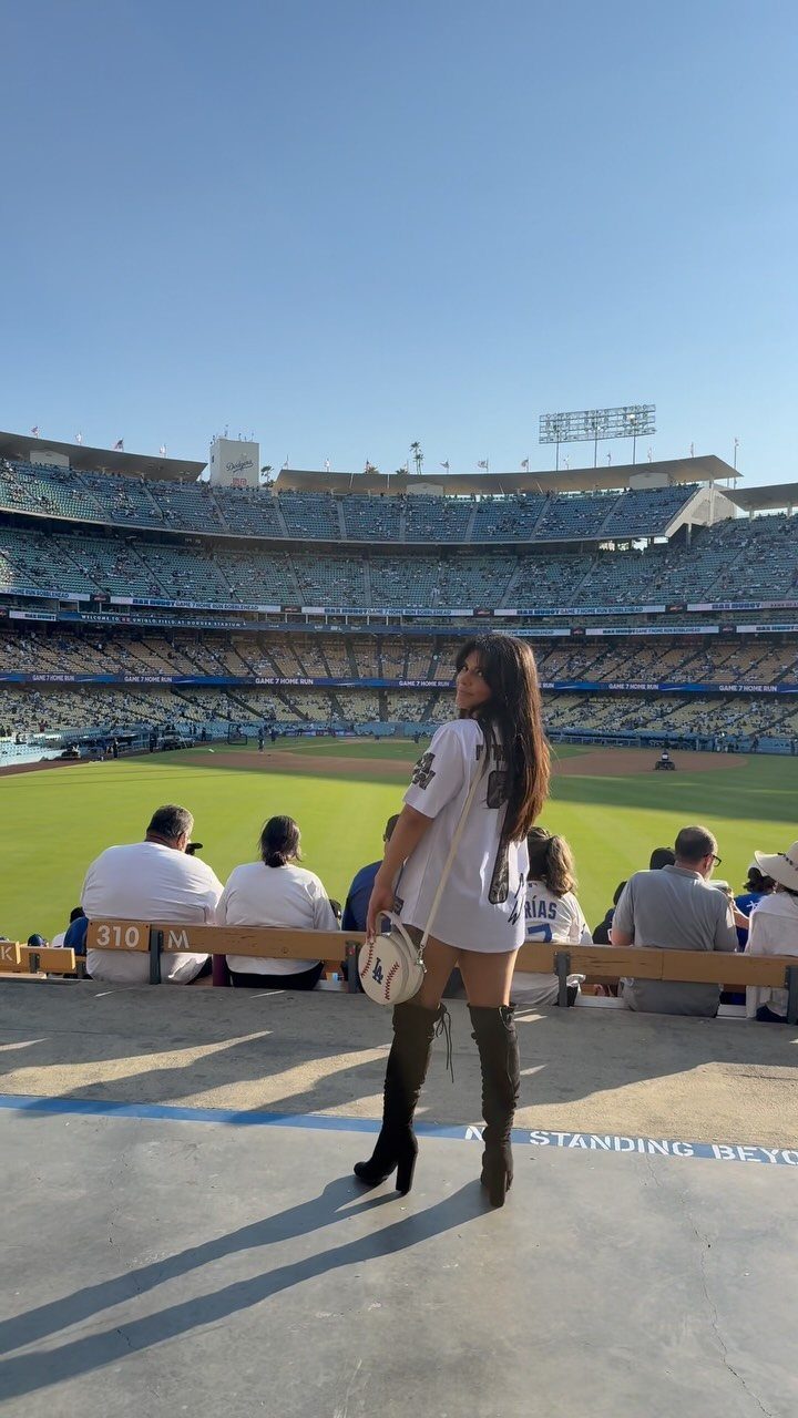 Woman in a white baseball jersey dress and olive green over-the-knee boots at stadium