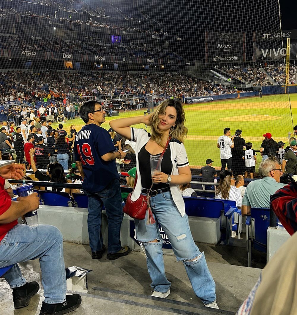 Woman in a black top and ripped blue jeans at a baseball stadium.