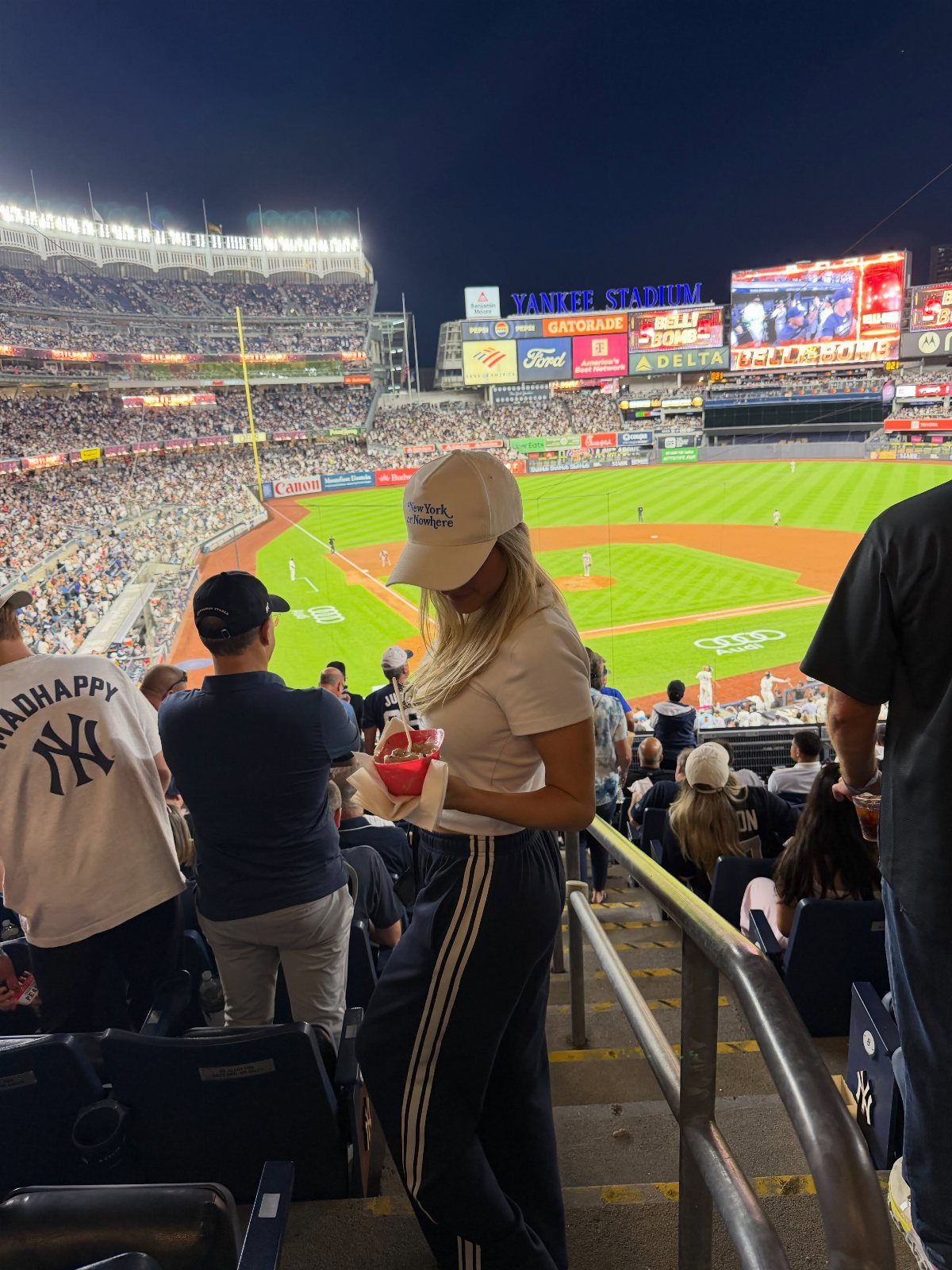 Woman in white t-shirt and black track pants at a baseball stadium.