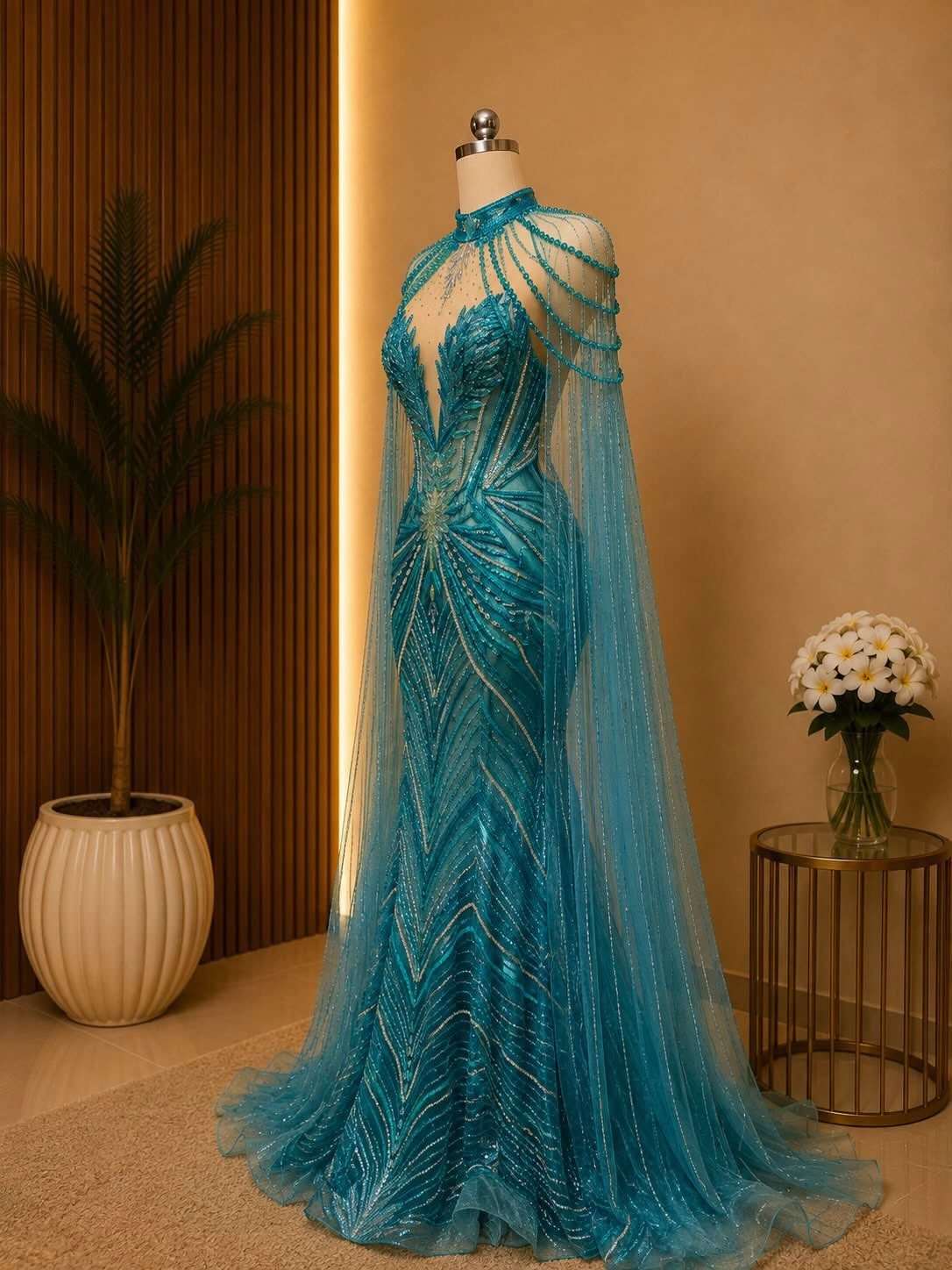 Turquoise blue beaded evening gown with a cape on a mannequin.