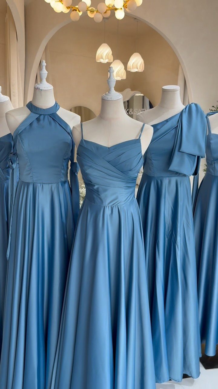 Three blue satin gowns on mannequins with different necklines in a bright room.