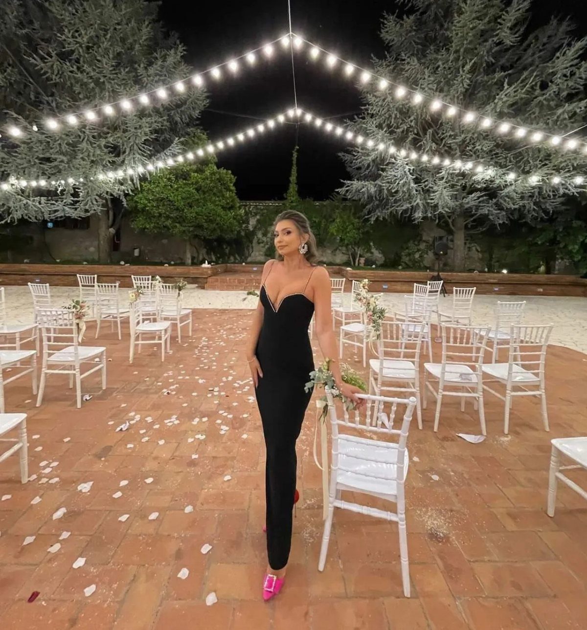 5 Blackout Party Outfits for a Night of Head-to-Toe Black 4 Woman in a long black party dress and pink heels in a courtyard
