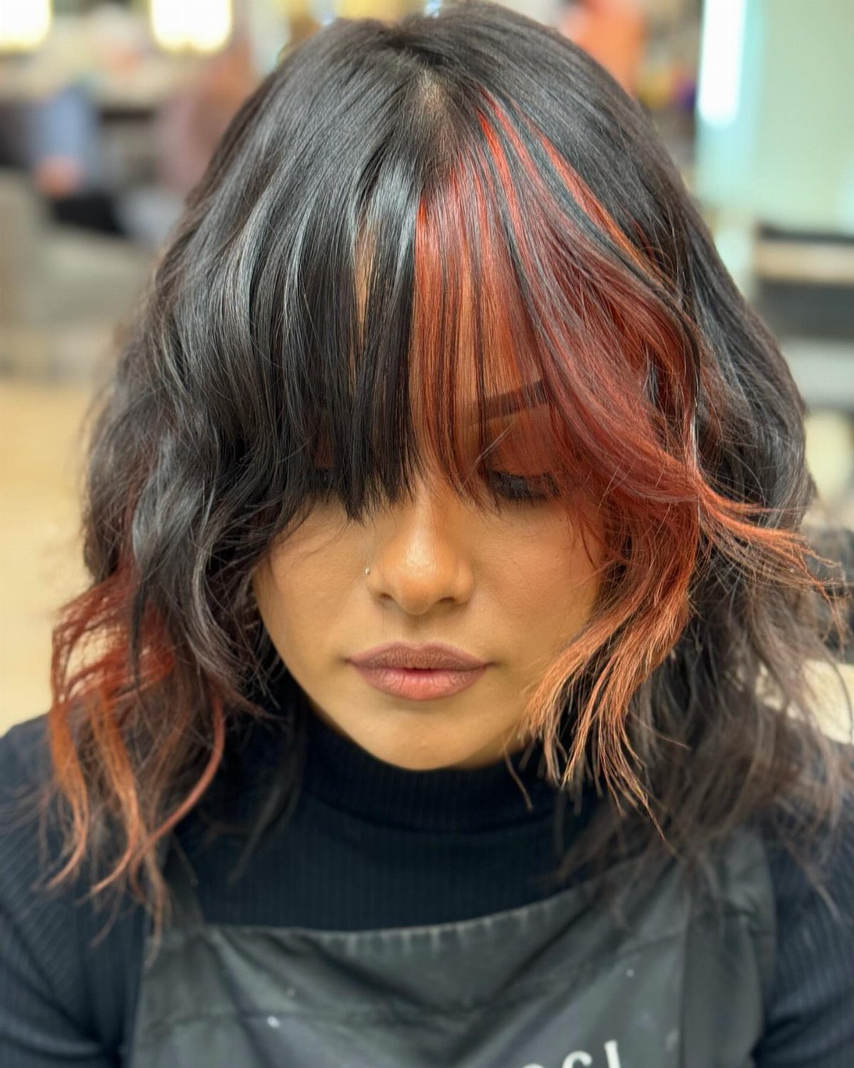 Woman with dark hair and bold red-orange color-blocked bangs and side sections.
