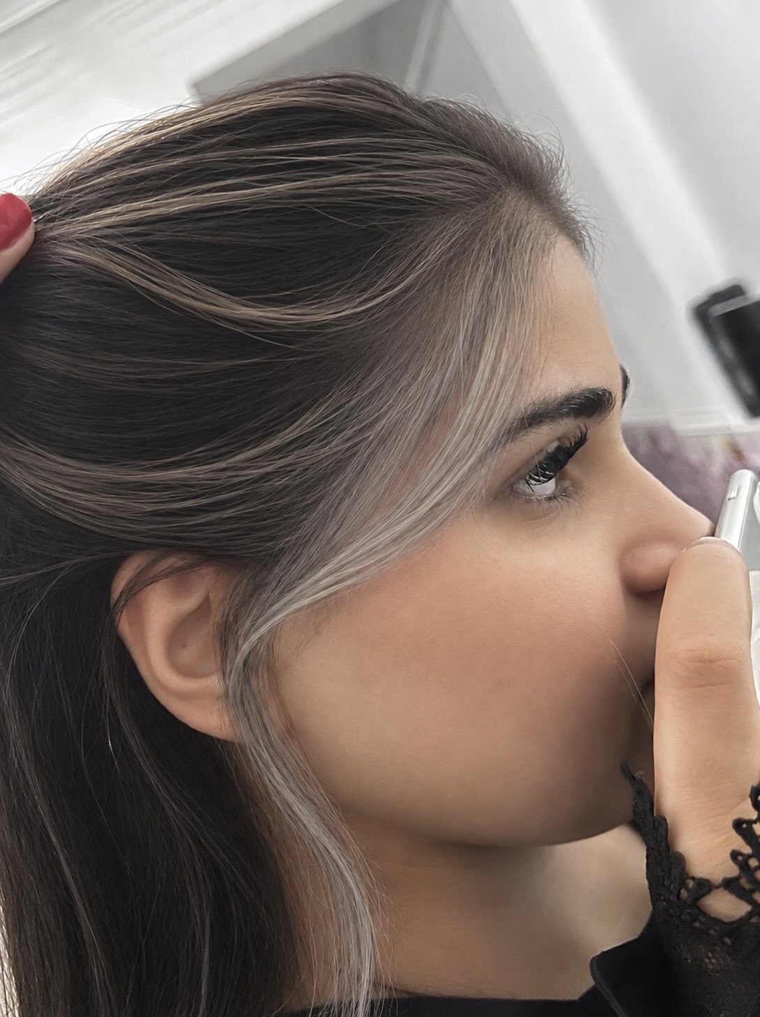Woman with dark hair and a silver-grey face-framing highlight applying lip makeup.