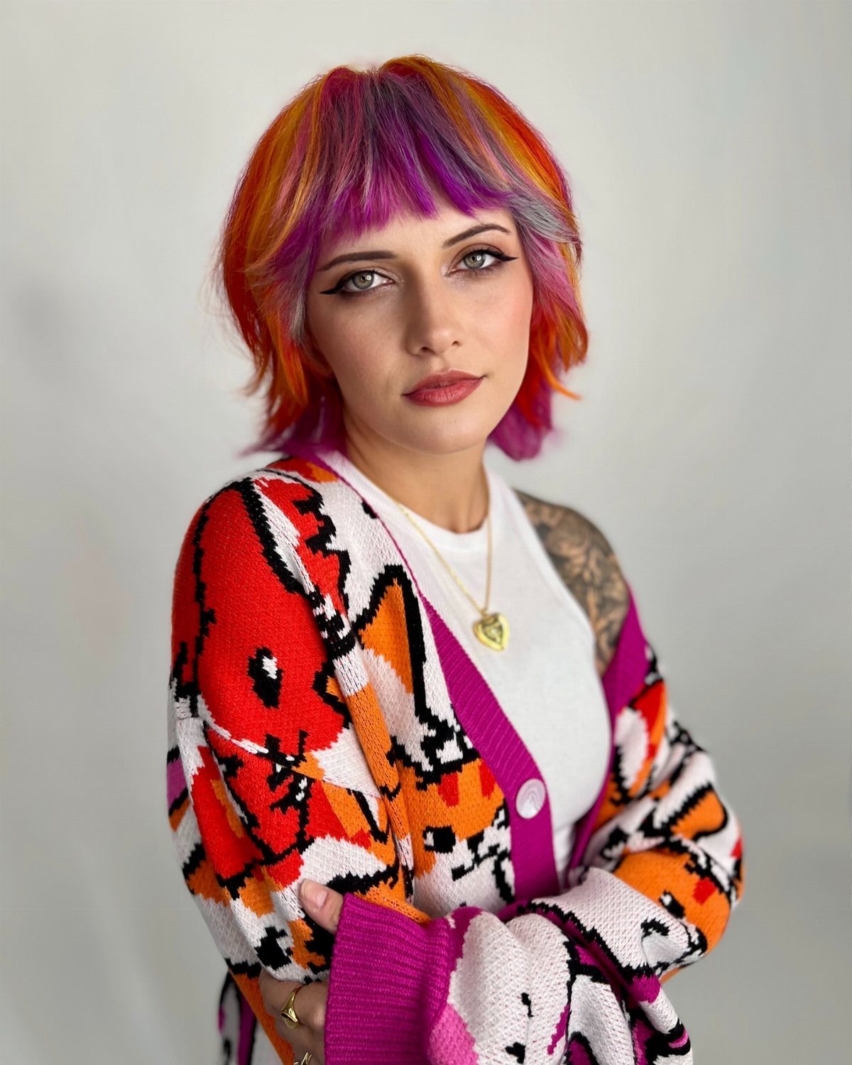Woman with multi-colored purple and orange block hair wearing a patterned cardigan.