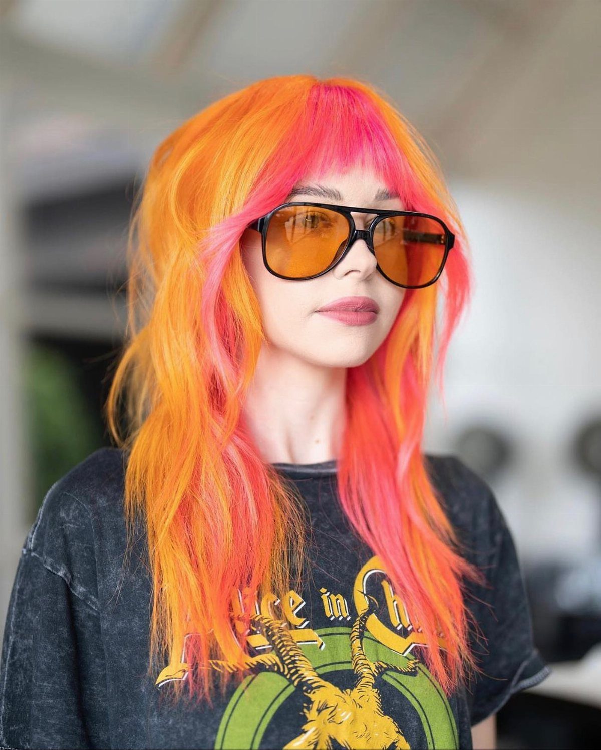 Person with vibrant orange and pink color-blocked hair wearing yellow-tinted sunglasses.