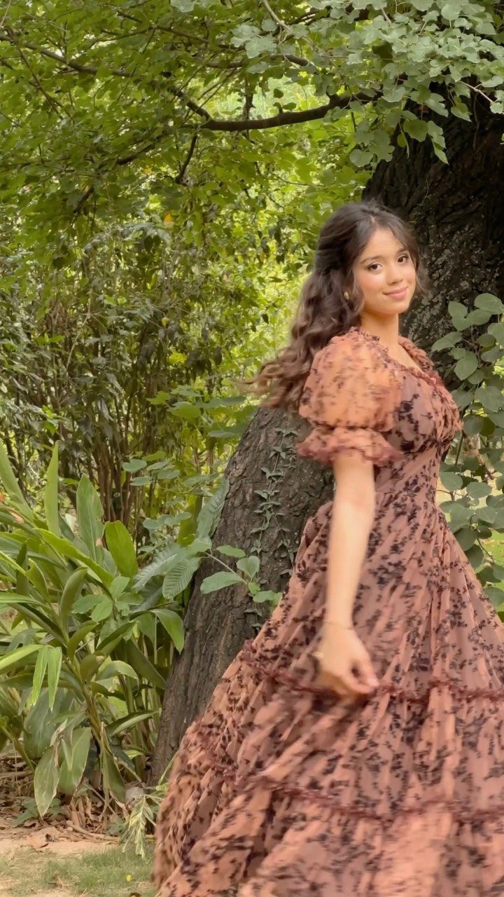 Woman in a brown floral puff-sleeved dress posing by a tree in a garden
