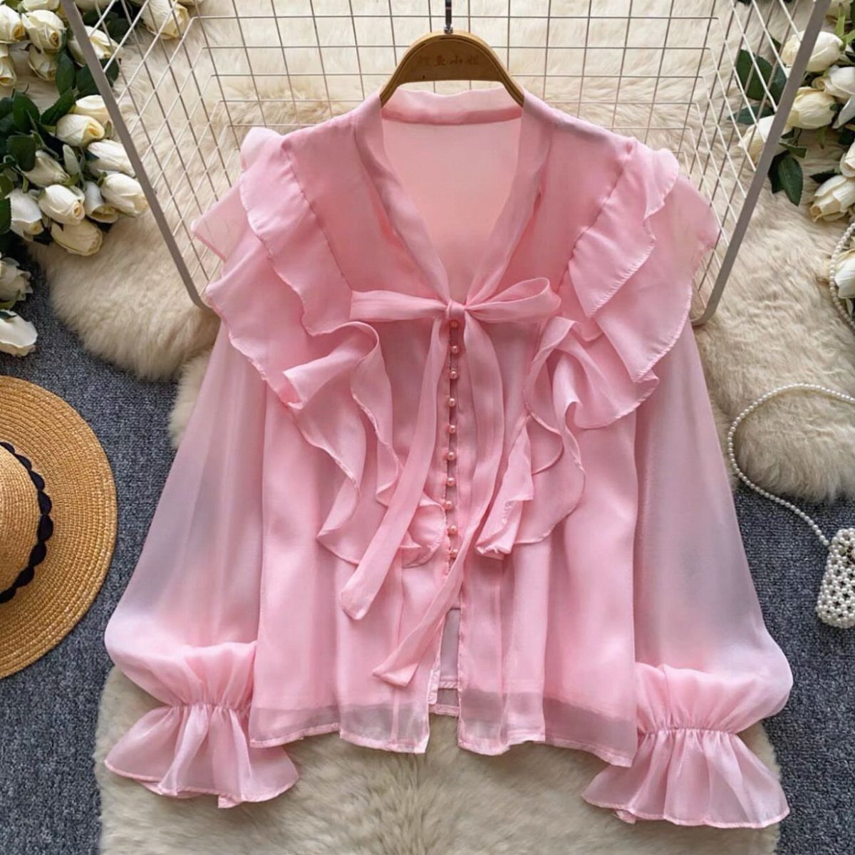 Pink ruffled blouse with a bow tie hanging over a white faux-fur rug
