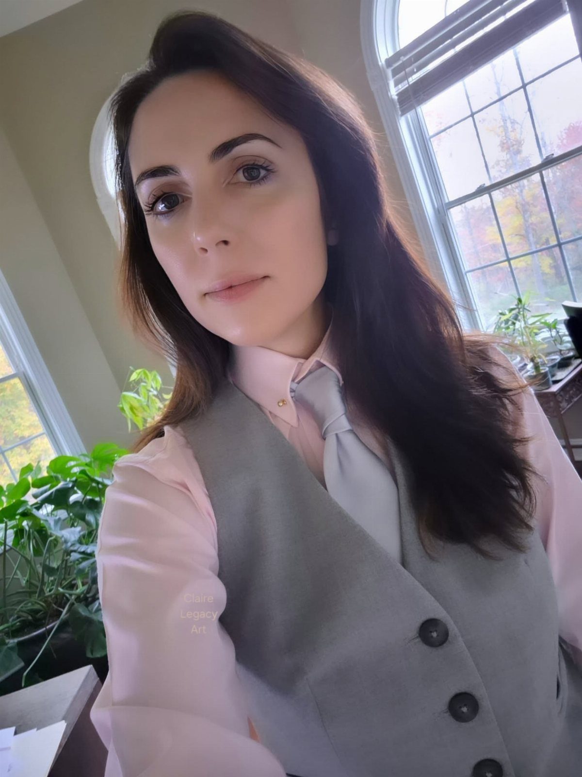 Woman wearing a pink shirt, grey tie, and grey waistcoat indoors near windows.