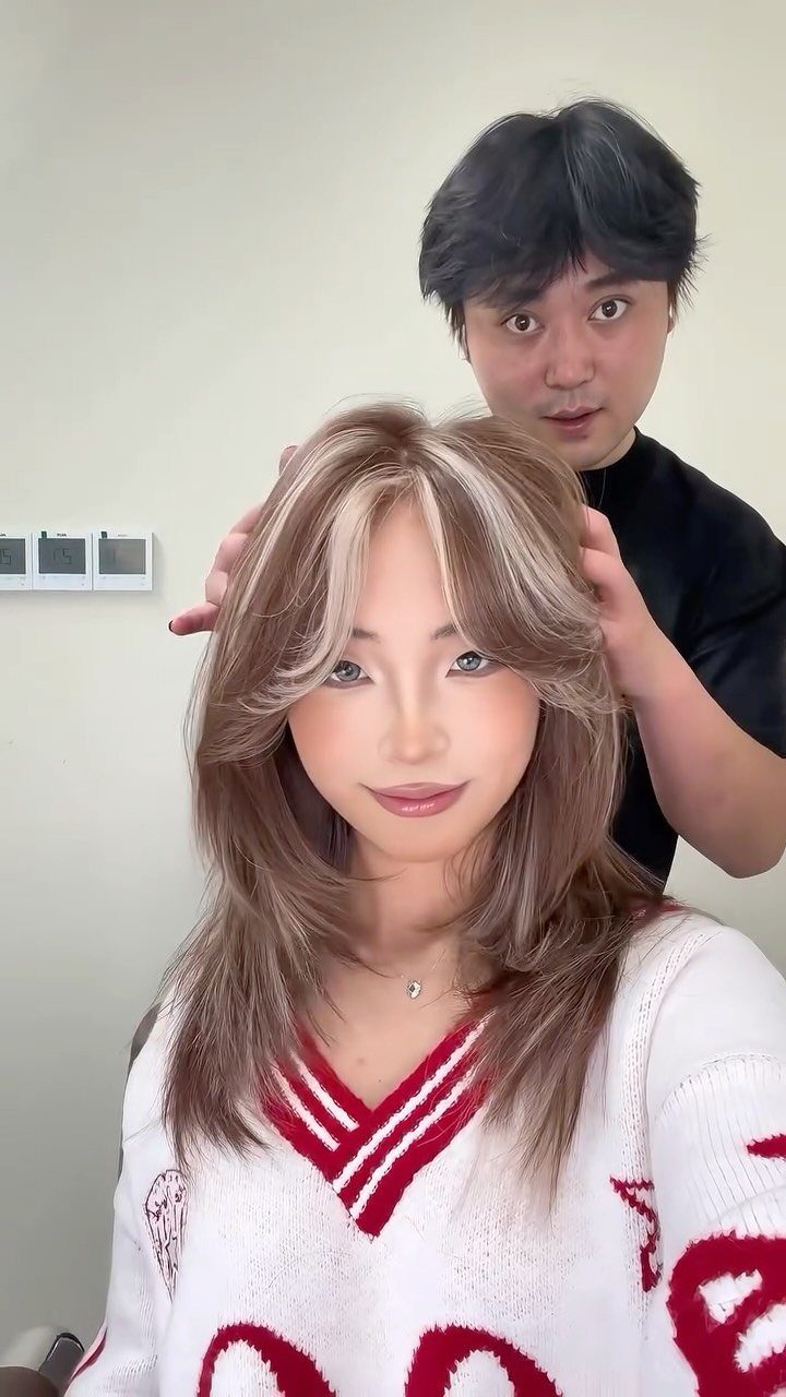 Woman with blonde money piece highlights and brown hair posing with a stylist.